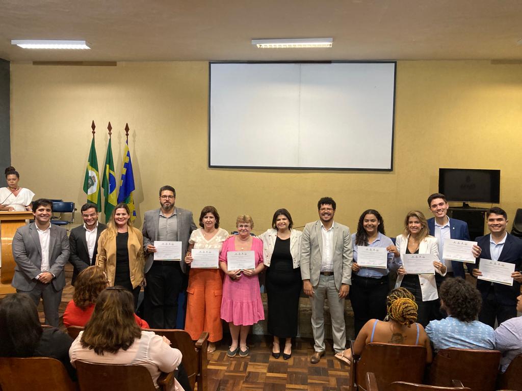 Empossados do Conselho Gestor do Escritório Popular da Juventude João Nogueira Jucá posam para foto enfileirados mostrando certificado.