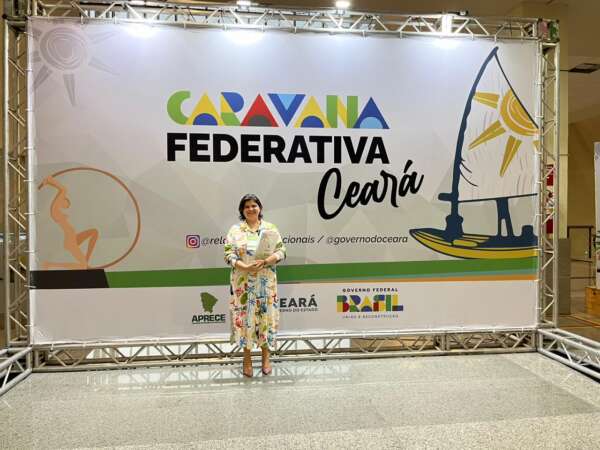 A secretária Adelita Monteiro posa diante do banner da Caravana Federativa do Ceará.